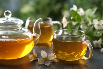 Tasty jasmine tea in cups, teapot and flowers on black table, closeup