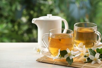 Tasty jasmine tea in cups, teapot and flowers at white wooden table, closeup. Space for text