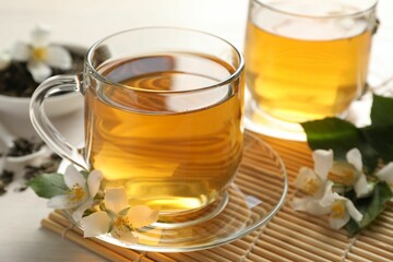 Tasty jasmine tea in cups, dry leaves and flowers on white wooden table, closeup
