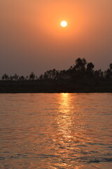 Naklejka premium Sindh Of Autumn River Landscape Or asia Part Of Pakista At Sunset. Sun Shine Over Blue Water Lake Or River At Sunrise. Nature At Sunny Morning. Woods With Orange Foliage On Riverside