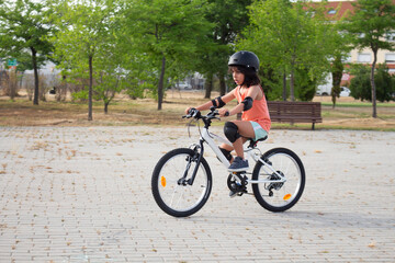Young girl riding bicycle wearing helmet and protections in a park