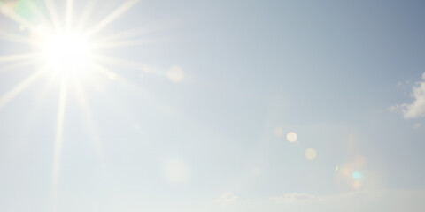 A bright sun shining in a pale blue sky with a few clouds and lens flares visible today