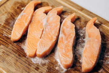 Raw salmon cut into steaks lies on a wooden cutting board in the kitchen with a slice of lemon.