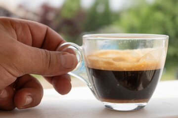 Hand holding a glass cup of espresso coffee with crema