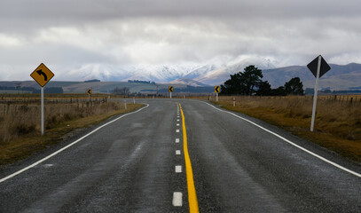 Winding Road sign along the road. Snow-capped mountains in the distance. Central Otago. South...
