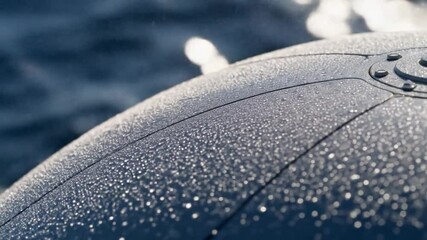Close-up of a wet, metallic surface with water droplets, possibly a boat or vehicle, with blurred water background. - Powered by Adobe