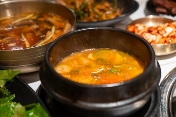 Kimchi Soup served in a bowl, with Korean side dishes served on the table