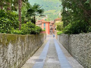 Narrow cobblestone Via alla Torre walkway between moss-cloaked stone walls and lush Mediterranean...