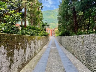 Narrow cobblestone Via alla Torre walkway between moss-cloaked stone walls and lush Mediterranean...