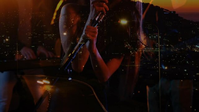 Female singer bringing mic to lips, singing, band playing rooftop gig with flickering city lights