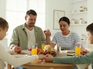 Family praying together before dinner at table indoors