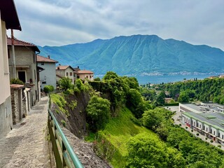 Hillside village in Lenno Ossuccio, with colorful houses, winding stone alleys, lush greenery, steep cliffs and panoramic view of church tower above the forested valley