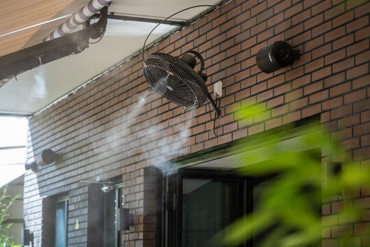 Water mist machine designed for creating coolness during heat and high temperature for comfort. Water spray system and fans working for cooling air in street cafe on hot sunny summer day close view