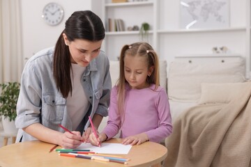 Mother teaching her daughter to draw at table indoors, space for text