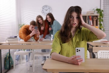 Teenage girl with smartphone suffering from bullying at school, selective focus