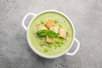 Tasty pea cream soup with croutons and basil on grey table, top view