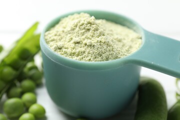 Protein powder in measuring spoon and green peas on table, closeup