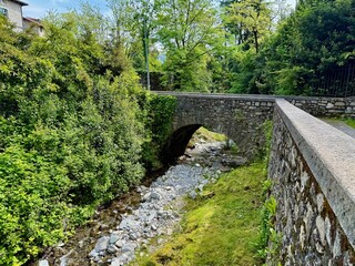 Historic stone arch bridge crossing rocky creek amid lush foliage along scenic Via Pola footpath near Lenno, Lake Como, Lombardy, northern Italy, rural landscape and heritage travel destination