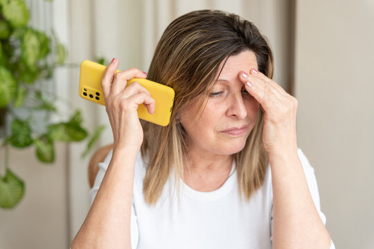 Senior woman experiencing stress and frustration while listening on her smartphone, touching her forehead with a worried expression