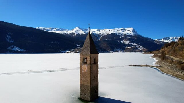 Church tower of Reschen - Vinschgau, South Tyrol - circling aerial view around the tower of the frozen white lake