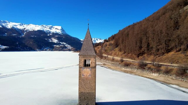 Church tower of Reschen - Vinschgau, South Tyrol - right-circling aerial photograph around the tower of the frozen white lake