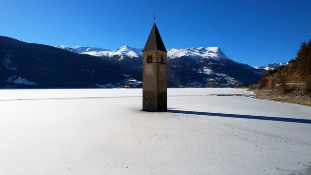 Church tower of Reschen - Vinschgau, South Tyrol - rising aerial view of the tower with a view of the frozen Lake Rechen
