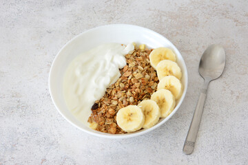 Granola, yogurt and banana slices in a white bowl top view healthy breakfast