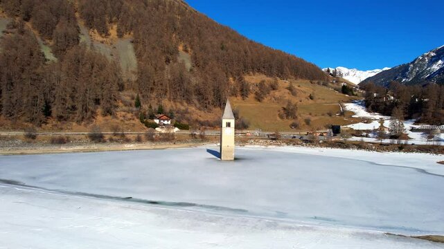 Church tower of Reschen - Vinschgau, South Tyrol - rising aerial view over the tower top from the frozen lake