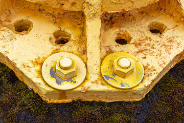 Close-up view of worn yellow bolts and nuts attached to a rusty metal structure, highlighting...