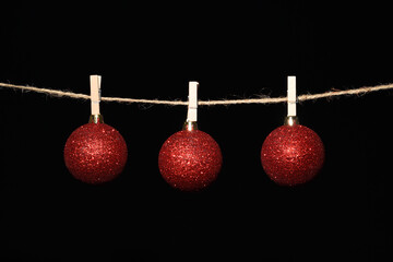 Bolas de navidad rojas colgadas con pinzas en una cuerda sobre fondo negro