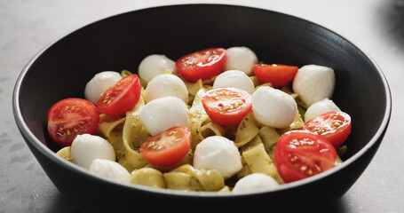 pesto fettuccine with mozzarella and tomatoes from black bowl on concrete countertop