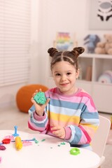 Motor skills development. Little girl playing with colorful dough at table indoors