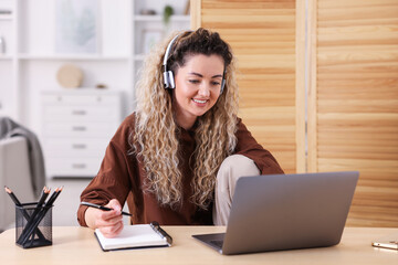 Smiling woman in headphones working with laptop at desk in home office