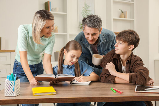 Parents and their children doing homework at table indoors