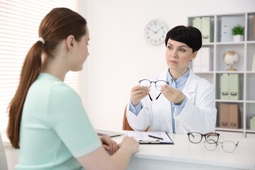 Fototapeta premium Ophthalmologist giving glasses to patient at white table in clinic