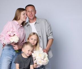 Family portrait of happy parents and their children with flowers on grey background. Space for text