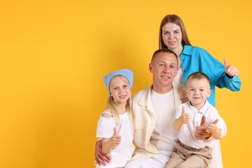 Family portrait of parents and their children showing thumbs up on yellow background. Space for text