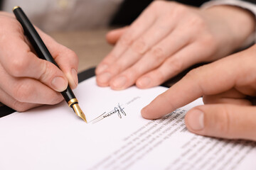 Man pointing at document and woman putting signature at table, closeup