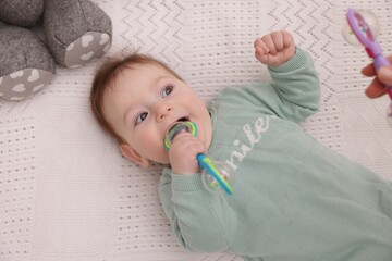 Mother and her cute little baby with rattle toy on bed at home, above view