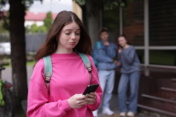 Teenage girl with smartphone suffering from bullying at school, selective focus