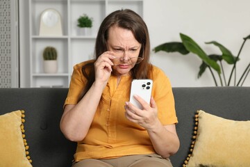 Woman with vision problem using smartphone on sofa at home