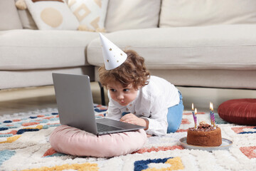 Birthday celebration. Little boy with cake having video call via laptop at home
