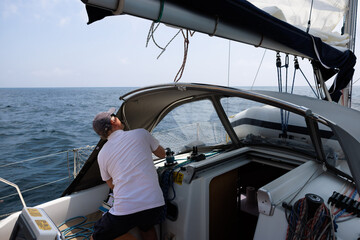 Mature man sailing in Costa Brava, adjusting sails on sailboat on sunny summer day