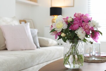 Bouquet of beautiful peonies and water on coffee table indoors, closeup with space for text. Interior design