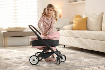 Cute little girl with doll stroller at home