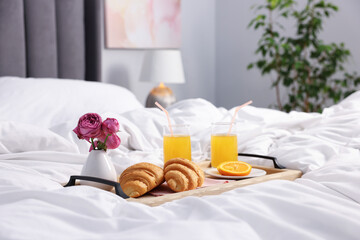 Tray with delicious breakfast and flowers on bed indoors. Space for text