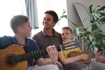 Happy father and sons playing guitars together and smiling at home