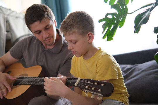 Father teaching his son to play guitar at home, family bonding