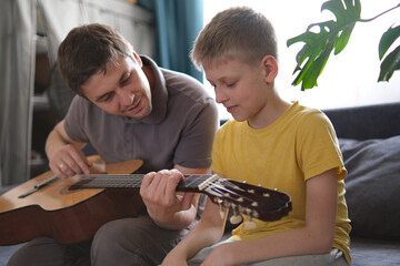 Father teaching his son to play guitar at home, family bonding