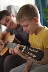 Father teaching his son to play guitar at home, family bonding